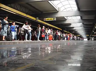 Multiple people wait at the long platforms of a station.