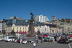A crowded city square, with cars and pedestrians