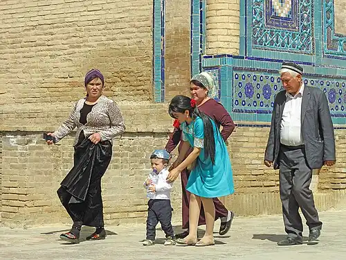 Uzbek women wearing contemporary traditional-style dresses and a man wearing a doʻppi