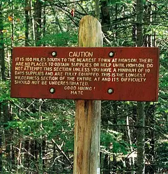 Wooden sign reading "Caution. It is 100 miles south to the nearest town at Monson. There are no places to obtain supplies or help until Monson. Do not attempt this section unless you have a minimum of 10 days supplies and are fully equipped. This is the longest wilderness section of the entire AT and its difficulty should not be underestimated. Good hiking! MATC"