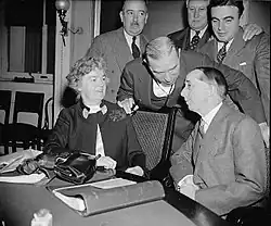 One civilian female sitting and six male civilians standing nearby