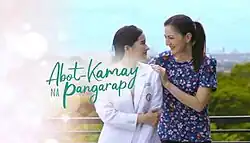 An image of Jillian Ward and Carmina Villarroel, looking at each other, with green trees and blue sky in the background and a pink gradient in the left side. The series title is displayed next to Ward.