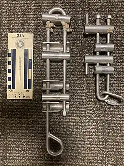 Two devices consisting of horizontal bars on a frame that a rope can be treaded around to provide friction. The one on the left is large, and has more bars than the one on the right, which has two longer bars too allow for additional friction to be added while rappelling