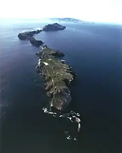 Aerial view of Anacapa with the lighthouse and coastguard station on East Anacapa in the foreground and Middle and West Anacapa behind. Santa Cruz Island is on the horizon.