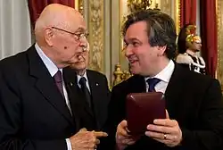 picture of elderly man to the left presenting a younger man to the right with an award