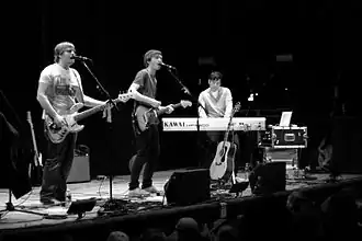 Several men performing onstage playing instruments and singing into a microphone