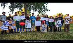Bangladeshis of all ages holding signs in front of a tree