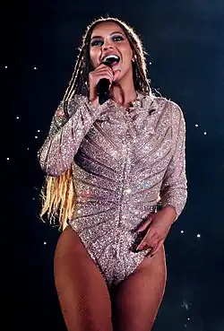 Beyoncé with box braids, wearing a silver glittery top, shouting into a microphone