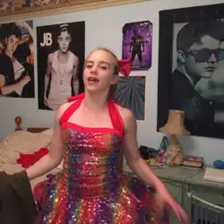 A photograph of Eilish wearing a rainbow-colored dress in front of a Justin Bieber-postered wall