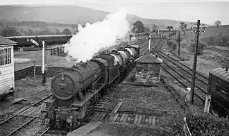 A steam train with freight wagons passing through a station