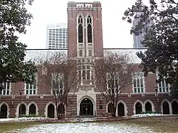 A wide, red brick building with a tower in the center and grey concrete archways spaced along the length of the building