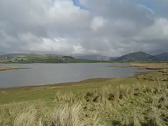 A view of Broad Water with grass in the foreground leading down to the shore , and hills in the background behind the lake.