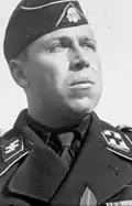 A man wearing a military uniform and side cap. His cap has an emblem in shape of a human skull and crossed bones.