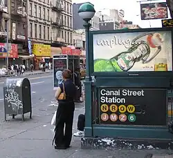 One of the station's entrances as seen in 2005. On the right, there is an advertisement above a sign with the words "Canal Street Station" and the emblems of the routes that stopped there. To the left of the sign, at the center of the image, is a pole with a green globe. The sidewalk and street are to the left.