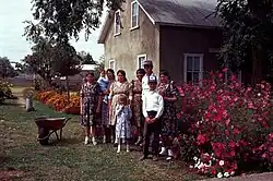 A Mennonite family, consisting of nine people, both children and adults, standing next to a flowerbed outside a house in Chihuahua, Mexico.