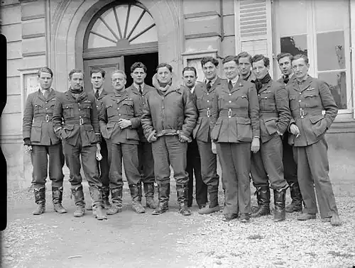 Thirteen men in dark military uniforms standing outside a building