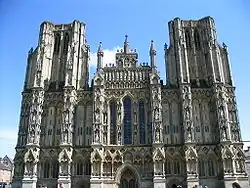 Large ornate grey stone facade of a building. Symmetrical with towers either side.