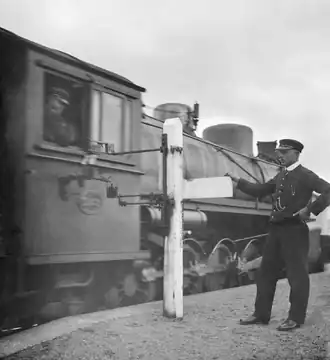 Exchanging signalling tablets, which authorise entry to the next section of track, between a moving X class locomotive and Horopito railway station in 1920.