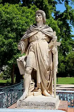 A middle aged man who wears a hauberk covered by coat and holds a sword