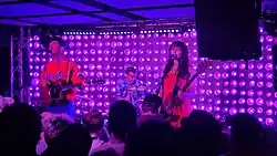 Against a bright purple backdrop, Cheekface performs in front of a crowded audience.