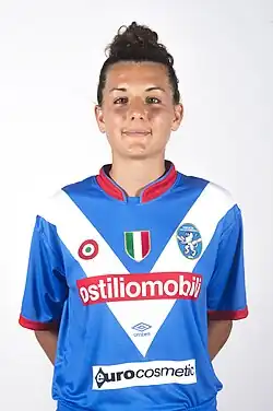 Woman with black hair in blue and white football kit.