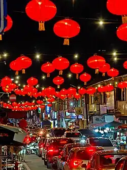 City street with heavy traffic, orange overhead lanterns, and mountains in the background