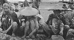 Black and white photograph of three Chinese men breaking large rocks with hammers
