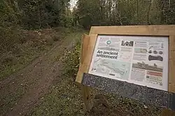 an informational sign stands by the side of an unpaved road in a wooded area