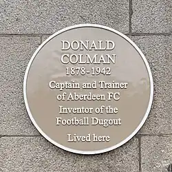 Circular, buff-coloured plaque with the text "Donald Colman 1878 -1942 Captain and Trainer of Aberdeen FC Inventor of the Football Dugout Lived Here
