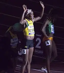 Thompson waving to a crowd while a spotlight is on her