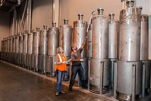 Each canister, 10-foot (3.0 m) tall and 2-foot (0.61 m) in diameter, weighing about 2 short tons (1.8 t), is stored at SRS Glass Waste Storage Building until a permanent repository is completed.