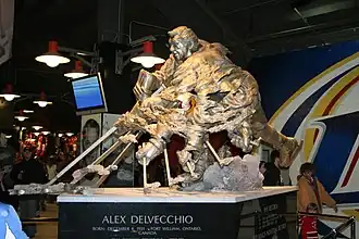 A large bronze statue of an ice hockey player in the act of shooting the puck. The player's hands and stick are shown numerous times to simulate motion. At the base of the statue is inscribed "Alex Delvecchio Born: December 4, 1931, Fort William, Ontario, Canada