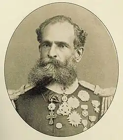 A photographic portrait of a dark-bearded man in heavily braided military tunic bedecked with many medals.