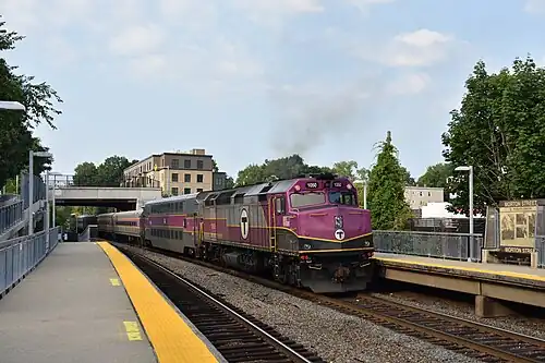A diesel locomotive pushing a passenger train out of an urban station
