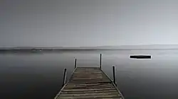 A dock extends from the shore of an extremely wide river.