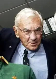 Heptagenerian caucasian male wearing a blue shirt, blazer and glasses; Springbols jersey in the foreground
