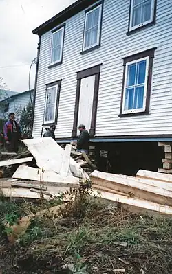 Three men are shown in the process of jacking up the foundation of a two-storey house