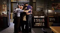 Several people in a group hug, visible from right to left: Paget Brewster as Frankie Dart, Jim Rash as Dean Pelton, Ken Jeung as Ben Chang, and Joel McHale as Jeffrey Winger.
