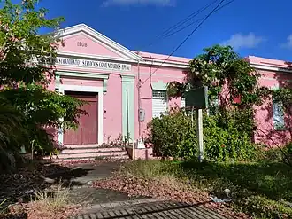 Photograph of the Derkes School, a disused, single-story, pink structure with a classical entry