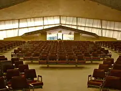 Westward view of the main sanctuary, looking toward the main entrance. There are seats in the foreground. The windows on the upper part of the base are visible in the background; these windows are slanted upward, and the entrance is visible beneath the peak of the windows.