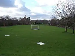 A long narrow strip of grass stretches into the distance, with houses on both sides. The grass is occupied by football pitches.