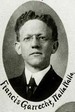 Black and white portrait photo of male with glasses dressed in suit