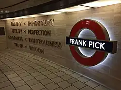 Words mounted on a cream-coloured stone wall next to a large, illuminated London Underground symbol (red ring with a blue bar) with the words "Frank Pick" on the blue bar