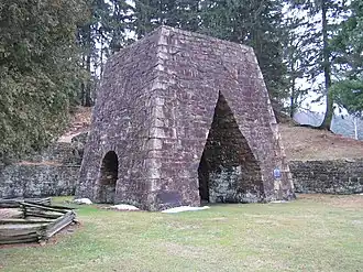 A large stone iron furnace with openings on each of the two sides visible