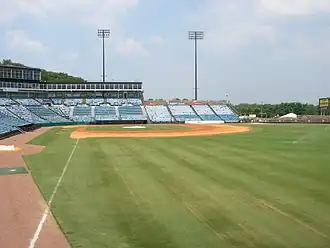A view from the right-field line of the seating bowl at Greer. Blue seats stretch from the right-field wall, behind home plate, and beyond the third-base dugout.