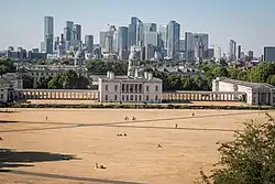 A city park with dry yellow grass, surrounded by a London cityscape.