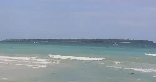 Long low green island, about 3.9 km (2 mi) distant. Two beaches can be made out.