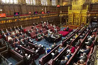 Wood-panelled room with high ceiling containing comfortable red padded benches and large gold throne