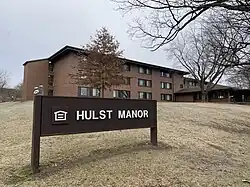 A building with a sign in the foreground reading "Hulst Manor"
