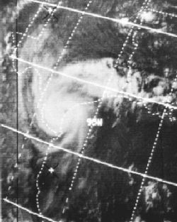 A black and white satellite image of a hurricane making landfall. The hurricane has a small faint eye and is located at the top left of the picture.